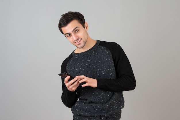 Retrato de hombre joven guapo posando con teléfono móvil sobre pared gris