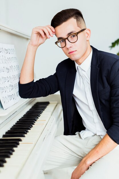 Retrato de hombre joven guapo sentado cerca del piano con hoja musical