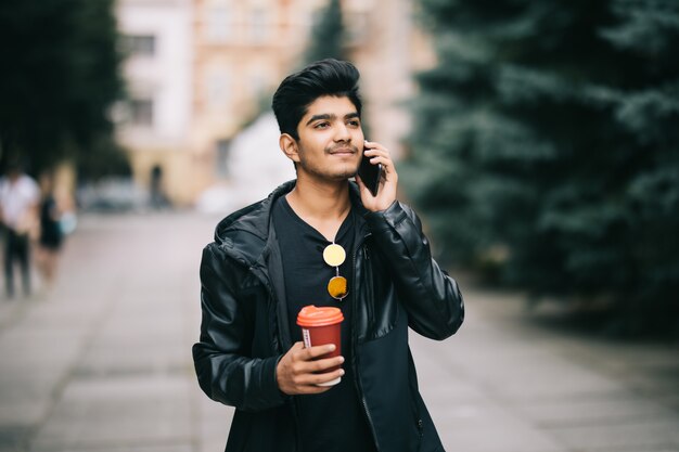 Retrato de hombre joven hablando por teléfono y caminando por la calle