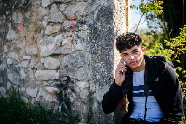Retrato de hombre joven hablando por teléfono celular cerca de muro de piedra