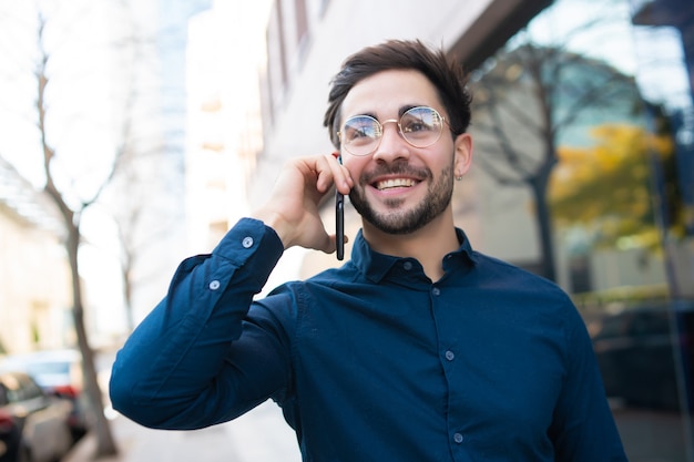 Retrato de hombre joven hablando por teléfono mientras camina al aire libre en la calle. Concepto urbano.