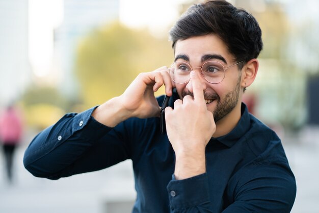 Retrato de hombre joven hablando por teléfono mientras está parado al aire libre en la calle. Concepto urbano.