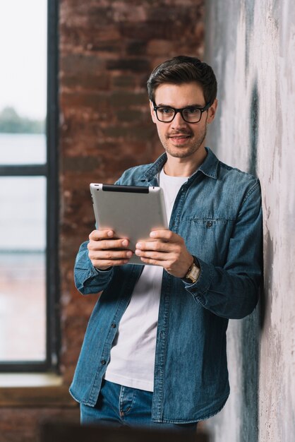 Retrato del hombre joven hermoso que sostiene la tableta digital en manos