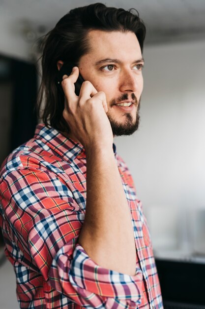 Retrato de un hombre joven inteligente en camisa a cuadros hablando por teléfono celular