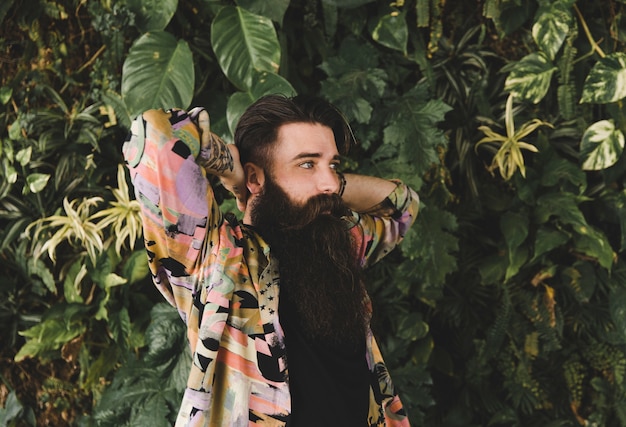 Retrato de un hombre joven con larga barba de pie contra las plantas verdes