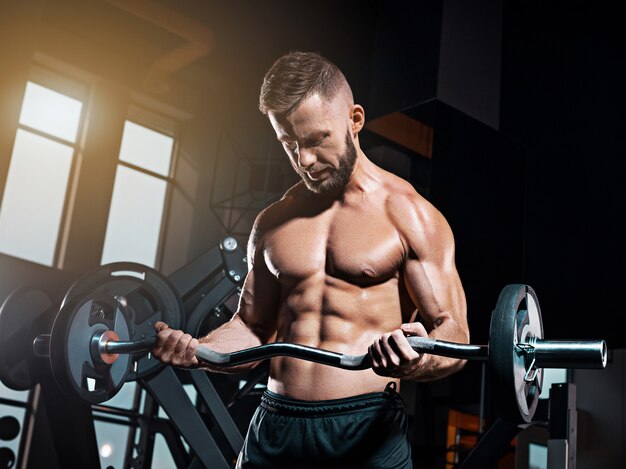 Retrato de hombre joven musculoso super fit trabajando en el gimnasio con barra