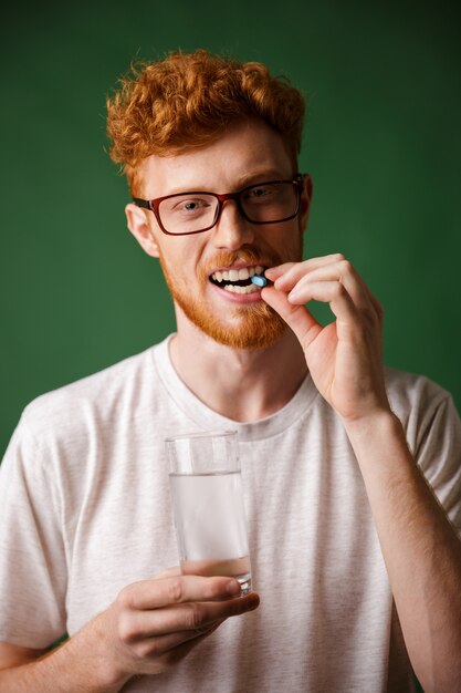 Retrato de un hombre joven pelirrojo en lentes mordiendo la píldora