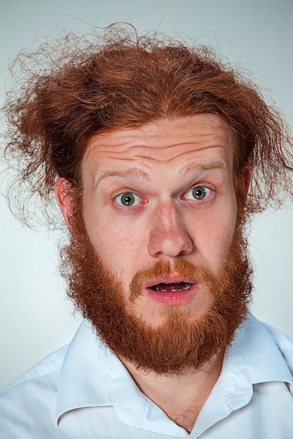 Foto gratuita retrato de hombre joven con pelo largo rojo y con expresión facial sorprendida sobre fondo gris