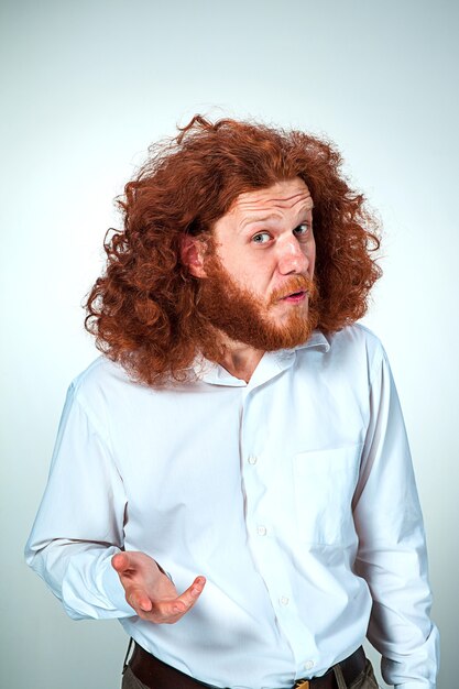Retrato de hombre joven con pelo largo rojo y con expresión facial sorprendida sobre fondo gris