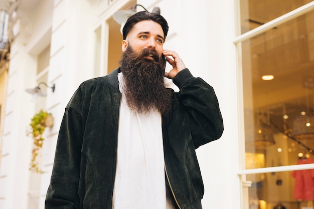 Foto gratuita retrato de un hombre joven de pie fuera de la tienda hablando por teléfono móvil