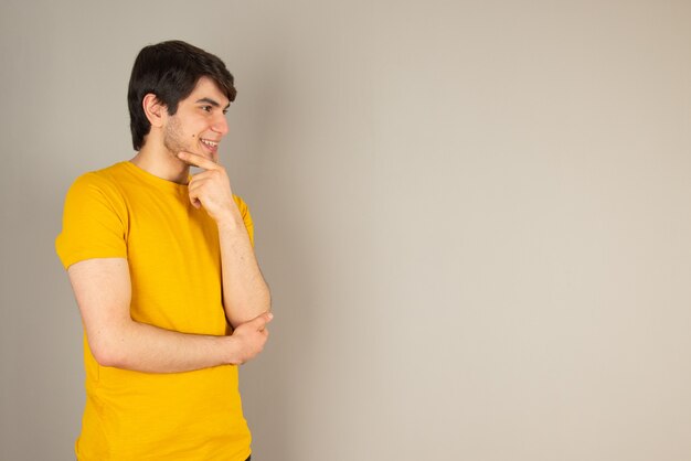 Retrato de un hombre joven de pie y mirando a otro lado contra el gris.