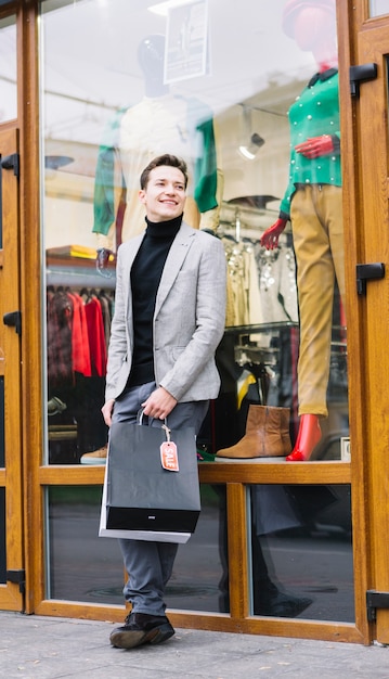 Retrato de un hombre joven que se coloca delante de la tienda que sostiene bolsos de compras