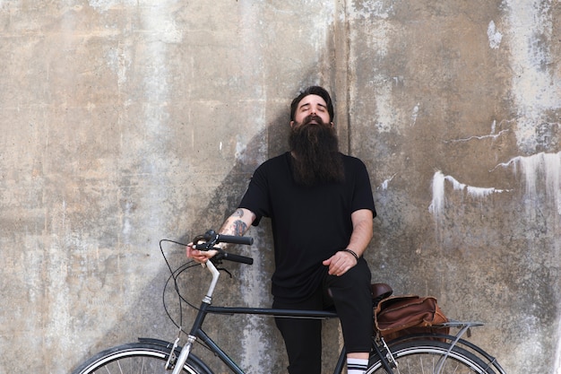 Foto gratuita retrato de un hombre joven que se inclina en la pared con la bicicleta