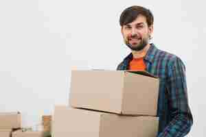 Foto gratuita retrato de un hombre joven que lleva las cajas de cartón que miran a la cámara contra el fondo blanco