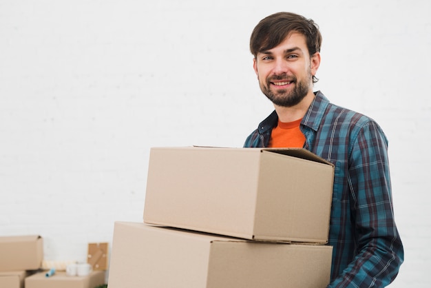 Retrato de un hombre joven que lleva las cajas de cartón que miran a la cámara contra el fondo blanco