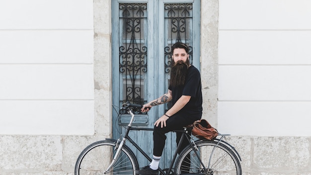 Foto gratuita retrato de un hombre joven que monta la bicicleta contra puerta cerrada