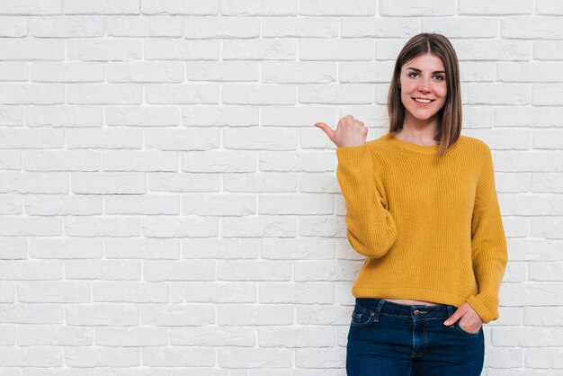 Retrato de un hombre joven que muestra el pulgar hacia arriba signo de pie contra la pared blanca