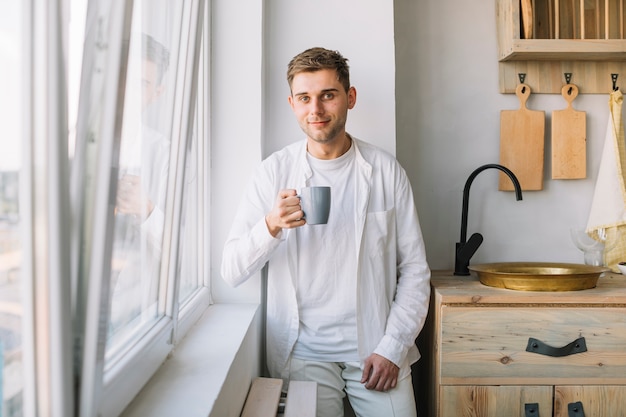 Retrato de un hombre joven que sostiene la taza de café que se coloca en cocina