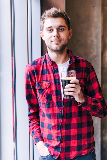 Retrato de un hombre joven que sostiene el vidrio de cerveza que mira la cámara