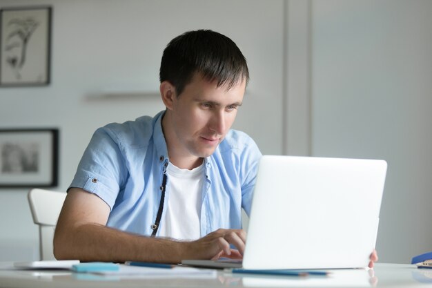 Retrato del hombre joven que trabaja en el escritorio con la computadora portátil
