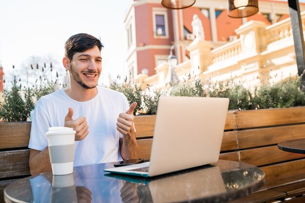 Retrato de un hombre joven que usa el chat de video de Skype portátil en la cafetería. Concepto de tecnología y Skype.