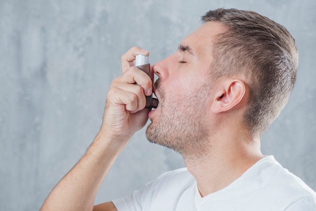 Retrato de un hombre joven que usa inhalador de asma contra el fondo gris