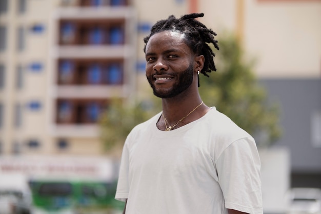 Retrato de hombre joven con rastas afro y camiseta blanca al aire libre