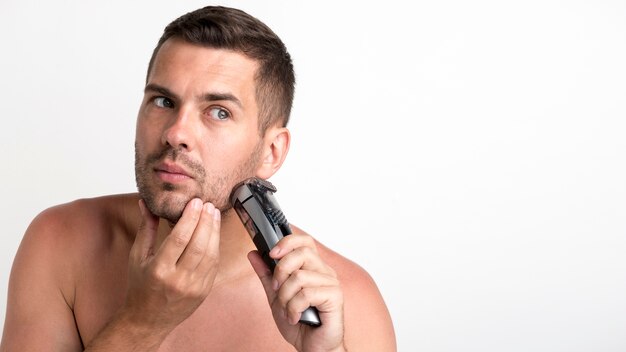 Retrato de hombre joven recortando su barba con recortadora