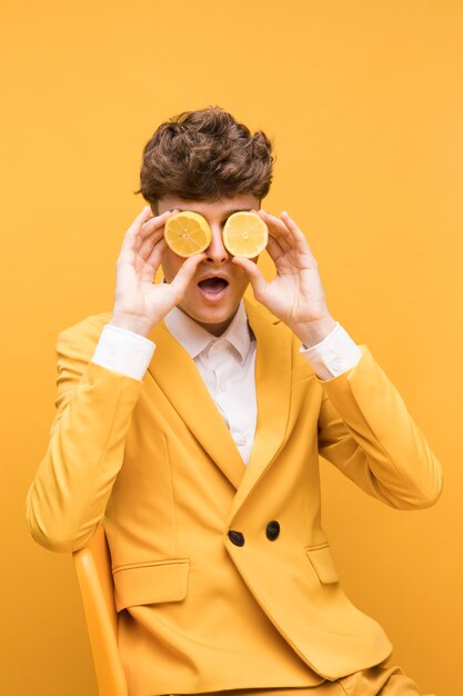 Retrato de hombre joven con rodajas de limón enfrente de los ojos en un escenario amarillo