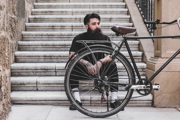 Retrato de un hombre joven sentado en la escalera con bicicleta