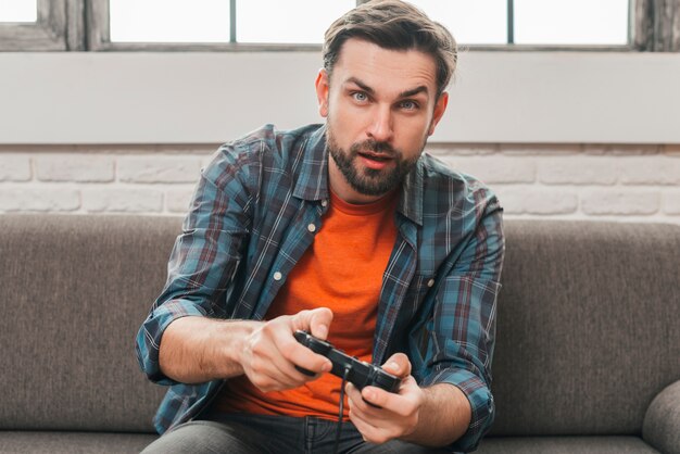 Retrato de un hombre joven sentado en el sofá jugando el videojuego