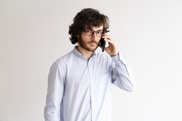 Retrato de hombre joven serio en gafas hablando por teléfono móvil.