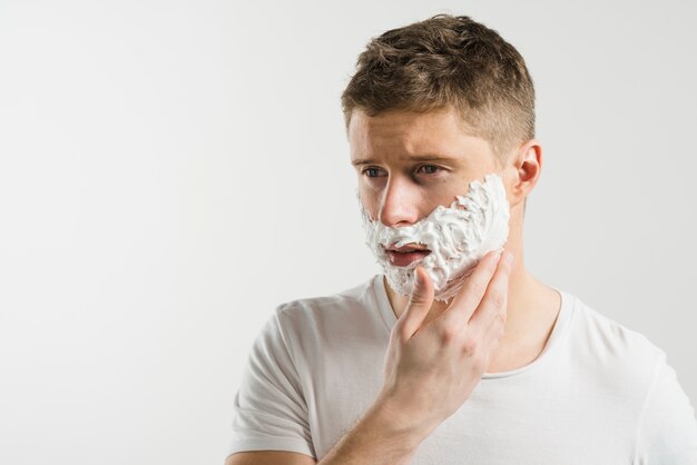 Retrato de un hombre joven serio que aplica espuma de afeitar en su mejilla