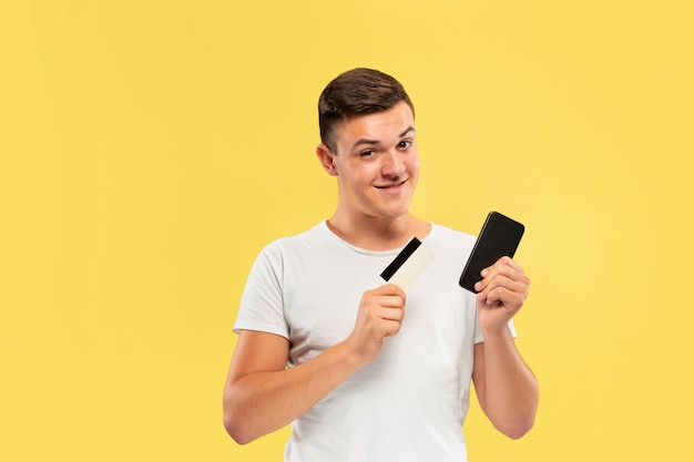 Retrato de hombre joven con smartphone y tarjeta de crédito aislado en la pared amarilla