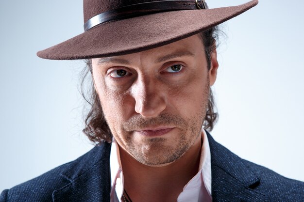 Retrato de hombre joven con sombrero en estudio gris.