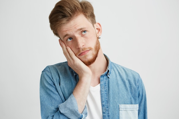 Retrato del hombre joven soñador que piensa mirando para arriba con la mano en mejilla.