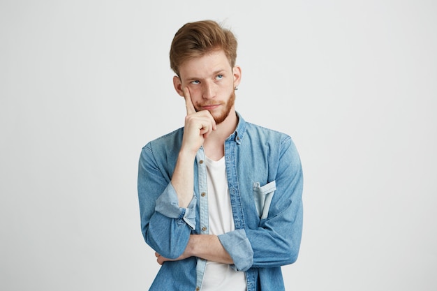 Retrato del hombre joven soñador que piensa mirando para arriba con la mano en mejilla.