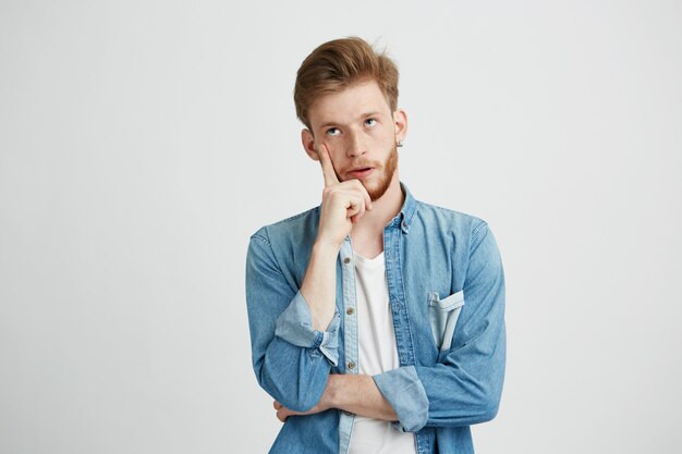 Retrato del hombre joven soñador que piensa mirando para arriba con la mano en mejilla.