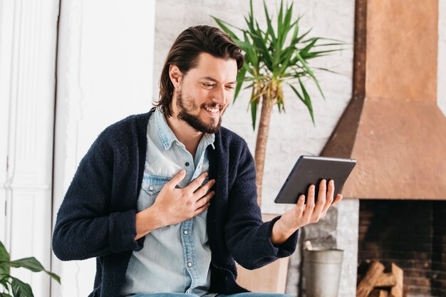 Retrato de un hombre joven sonriente que hace videollamada usando tableta digital