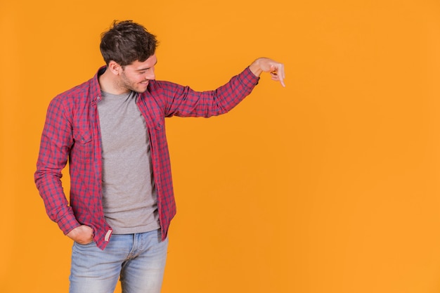 Retrato de un hombre joven sonriente que señala su dedo hacia abajo sobre un fondo naranja