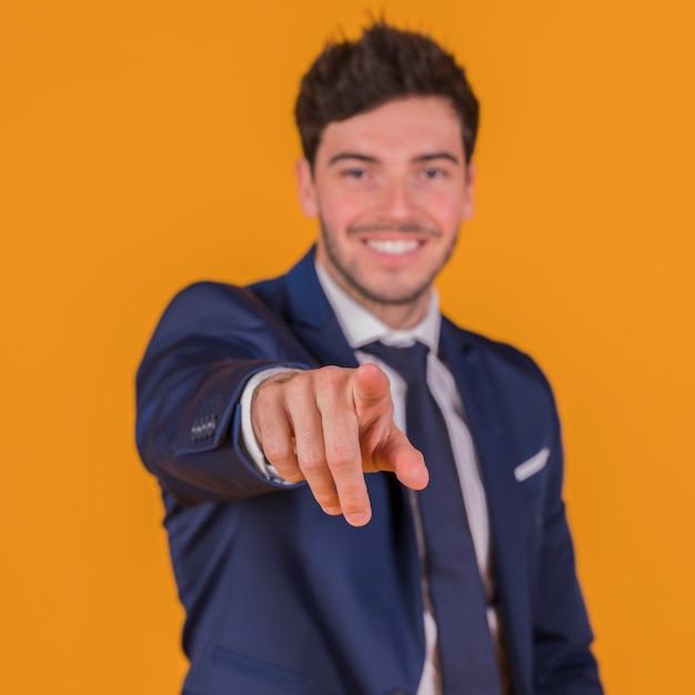 Retrato de un hombre joven sonriente que señala su dedo contra un fondo naranja