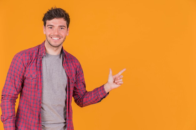 Retrato de un hombre joven sonriente que señala su dedo en un fondo anaranjado