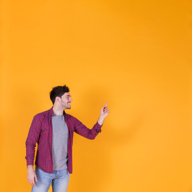 Retrato de un hombre joven sonriente que señala su dedo en un fondo anaranjado