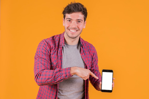 Retrato de un hombre joven sonriente que señala su dedo en el teléfono móvil contra un fondo anaranjado