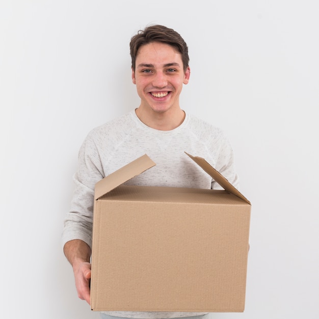 Retrato de un hombre joven sonriente que sostiene la caja de cartón contra el fondo blanco