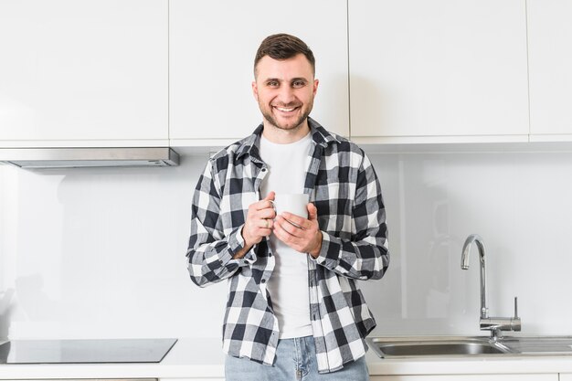 Retrato de un hombre joven sonriente que sostiene la taza en la mano mirando a la cámara