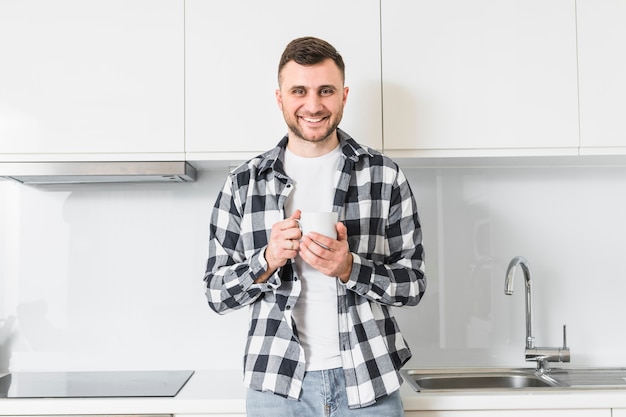 Retrato de un hombre joven sonriente que sostiene la taza en la mano mirando a la cámara