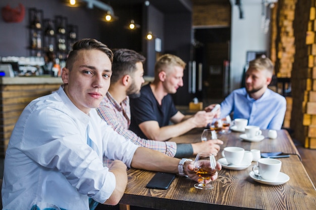 Foto gratuita retrato de hombre joven con sus amigos sosteniendo vaso de bebida