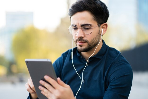 Retrato de hombre joven con tableta digital mientras está sentado en un banco al aire libre. Concepto urbano.