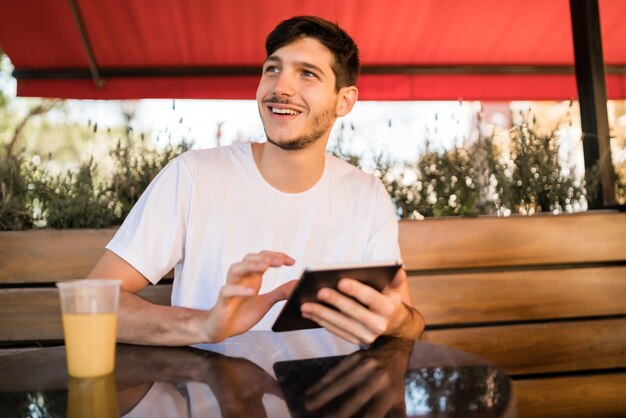 Retrato de hombre joven con una tableta digital mientras está sentado en una cafetería. Concepto de tecnología y estilo de vida.